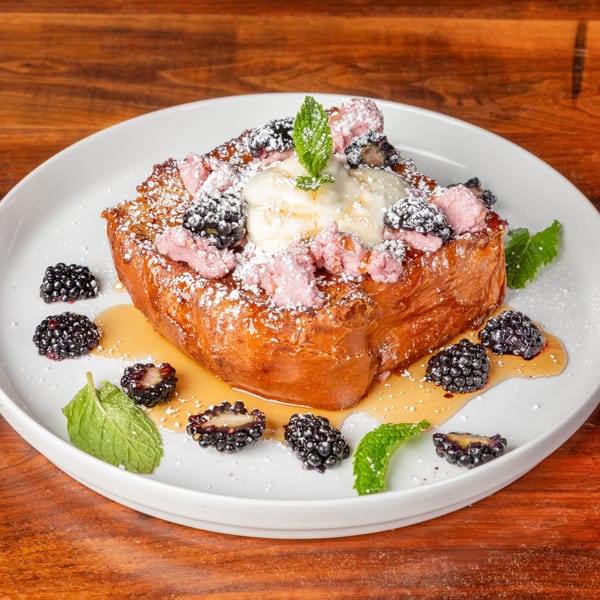 Golden French toast topped with vanilla ice cream, blackberries, pink meringue, and mint leaves.