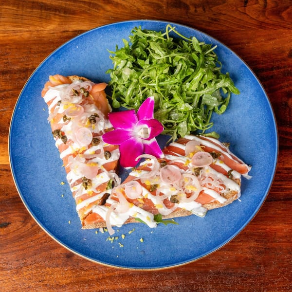 Smoked salmon flatbread with cream cheese, capers, onions, and arugula, garnished with an orchid.