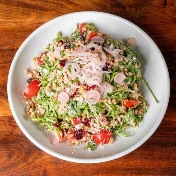 A vibrant salad with arugula, grains, cherry tomatoes, dried cranberries, and pickled onions.