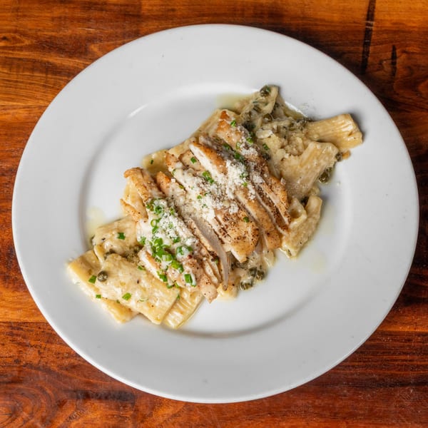 Creamy pasta with sliced chicken, capers, parmesan, and chives on a white plate.