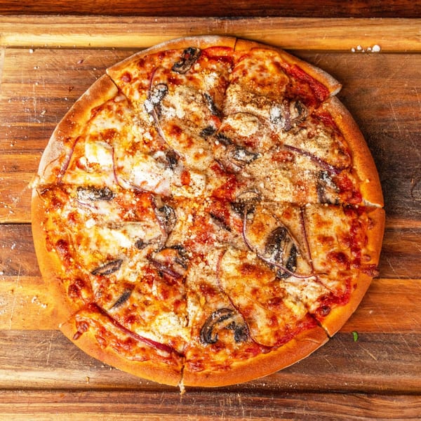 A whole mushroom and cheese pizza, with one slice removed, on a wooden cutting board.