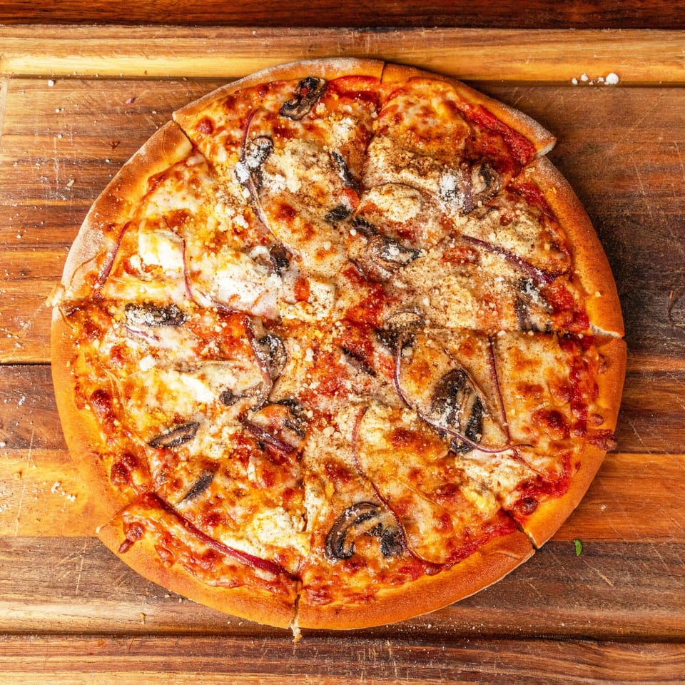 A whole mushroom and cheese pizza, with one slice removed, on a wooden cutting board.
