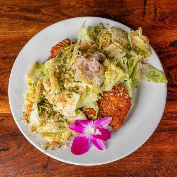 Crispy chicken cutlets and a fresh green salad with a purple orchid garnish on a white plate.