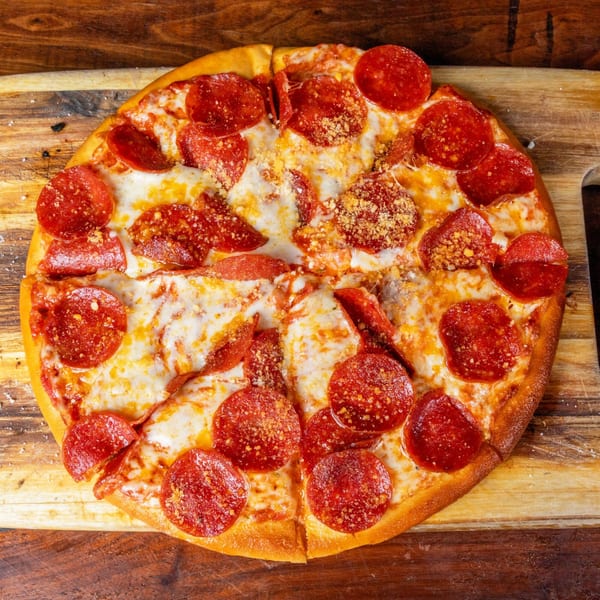 A freshly baked pepperoni pizza, sliced into eight pieces, on a rustic wooden cutting board.