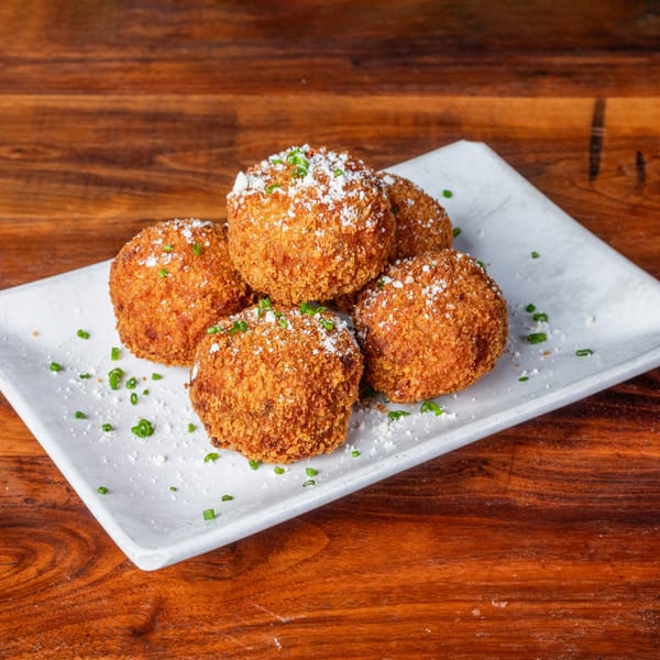 Five golden-brown arancini balls, sprinkled with white powder and green chives, on a white plate.